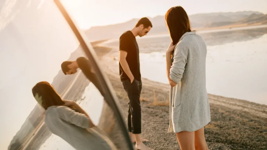 Couple dos à dos sur une plage au coucher du soleil, symbolisant la distance émotionnelle et la séparation après une rupture amoureuse