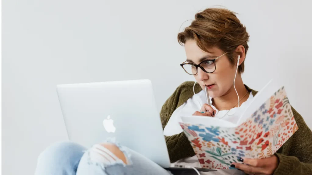 Femme en train de travailler sur un ordinateur avec un livre en pleine concentration