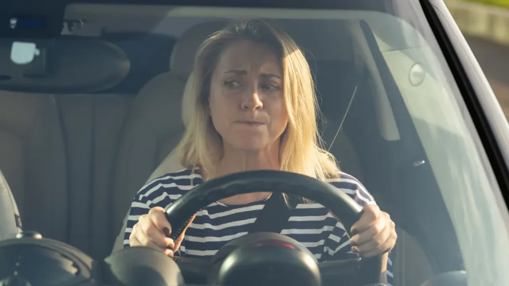Femme crispée au volant de sa voiture, mains serrées et regard anxieux illustrant l'amaxophobie